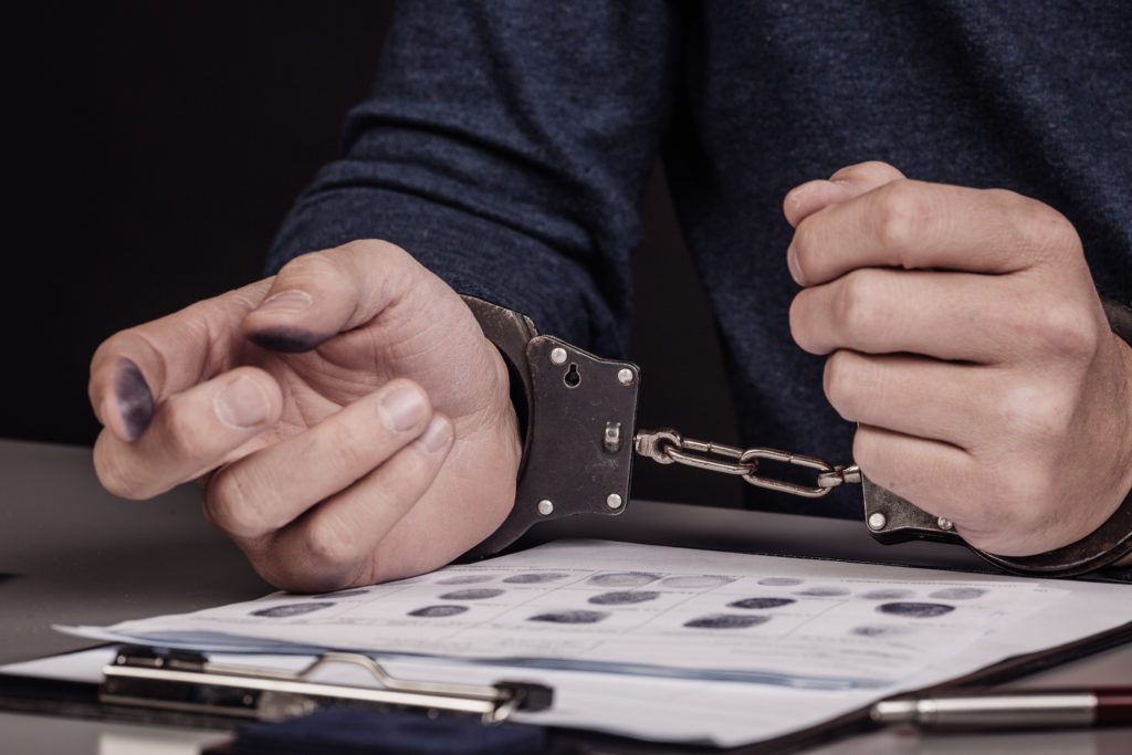 Protect Your Right During Arrest - hands with handcuffs lying on top of fingerprint sheets.